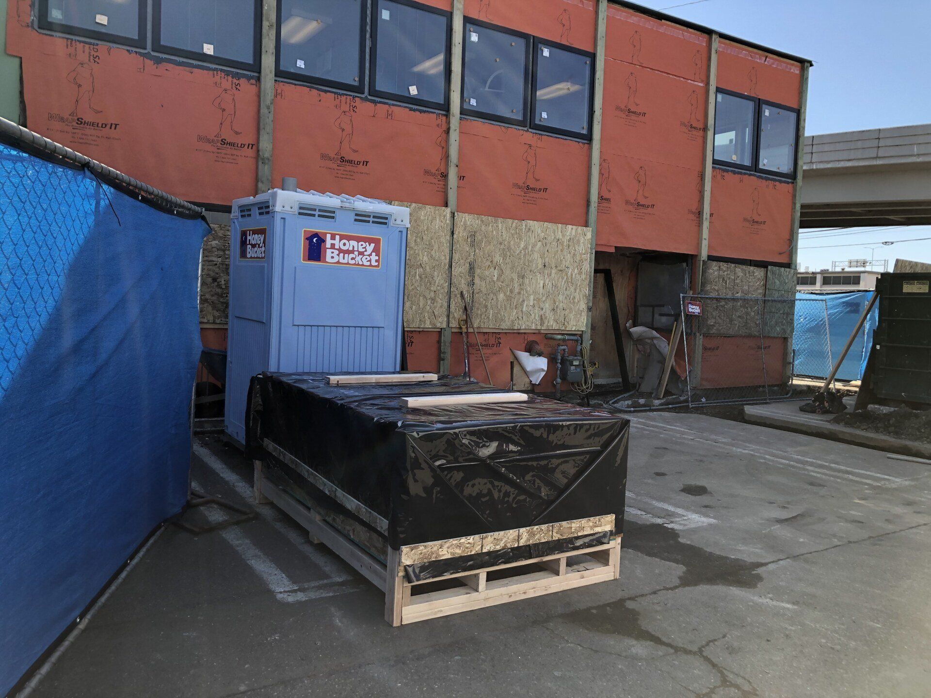 A portable toilet is sitting on a pallet in front of a building under construction.