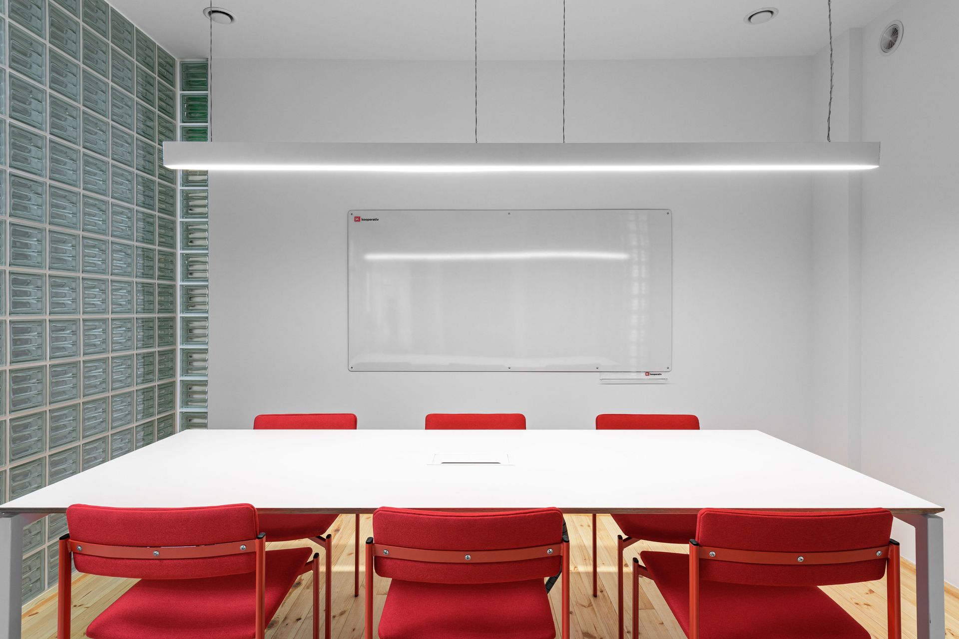 A conference room with a long white table and red chairs.