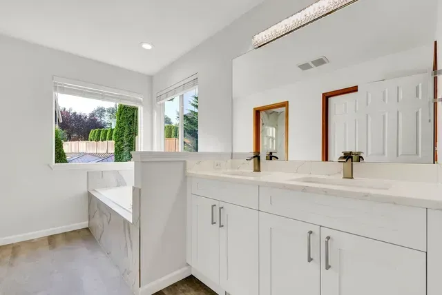 A bathroom with two sinks , two mirrors and a bathtub.