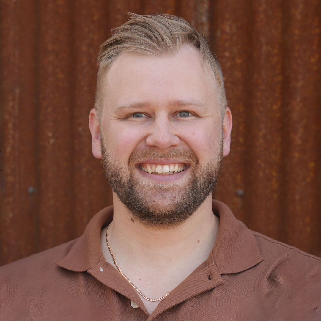 A man with a beard and mustache is standing in front of a tree.