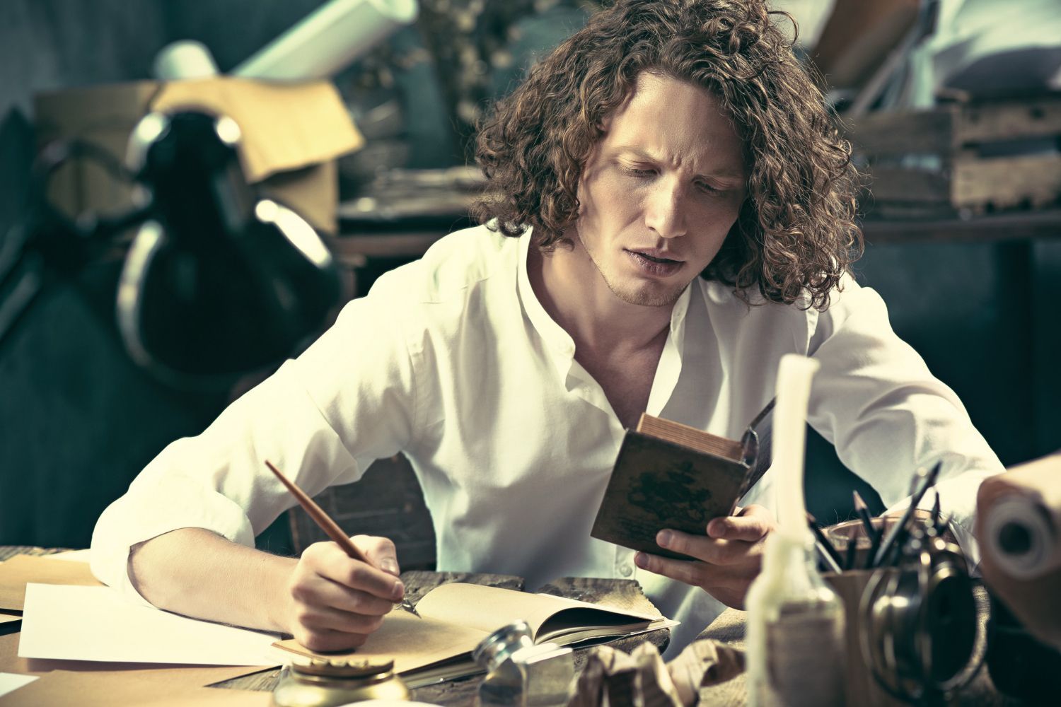 A man with curly hair is sitting at a table reading a book