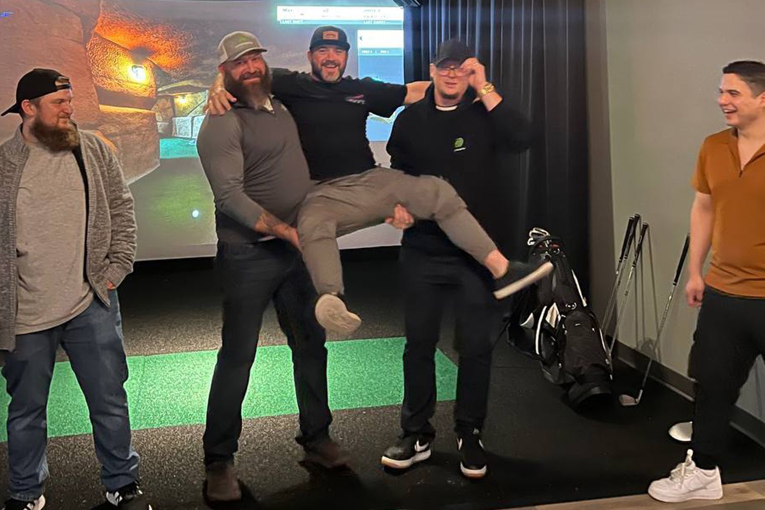 A group of men are posing for a picture while one man is carrying another man in his arms.