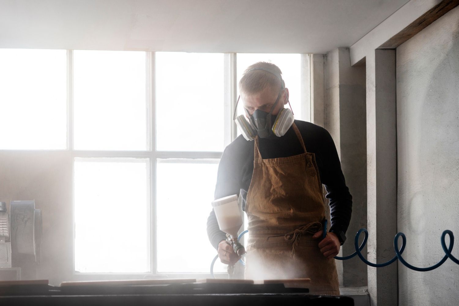 A man wearing a gas mask is painting a piece of wood.
