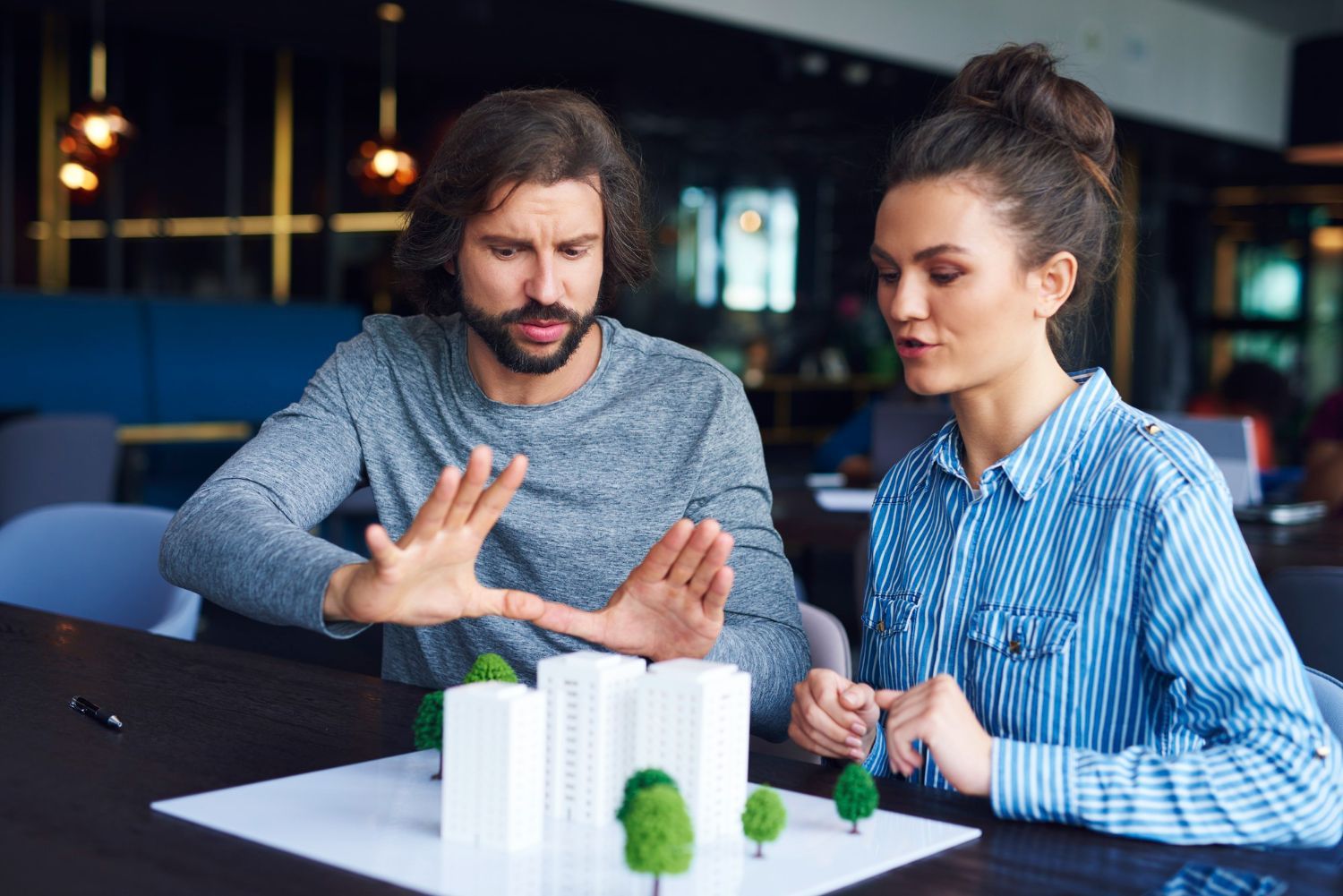 A man and a woman are sitting at a table looking at a model of a city.