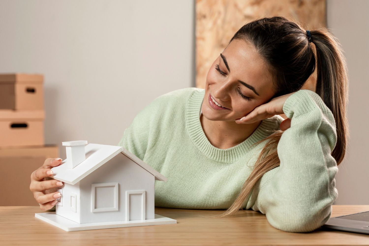 A woman is sitting at a table holding a model house.