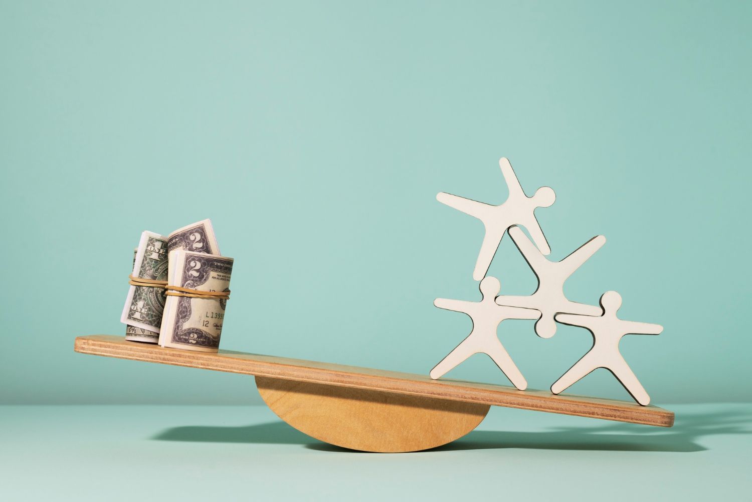 A wooden seesaw with a stack of money on it.