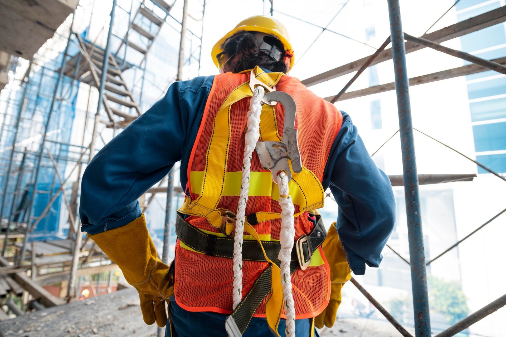 A construction worker wearing a safety vest and helmet is standing on a scaffolding.