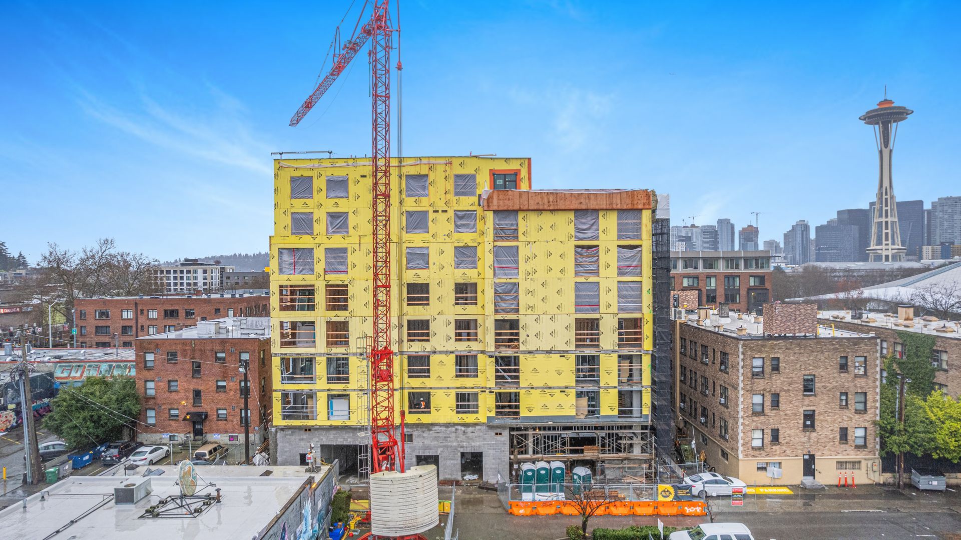A large yellow building is being built in a city with a crane in front of it.