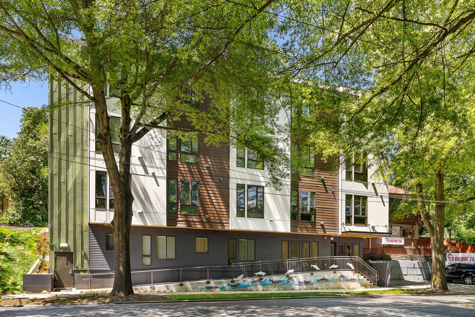A large apartment building with a pool in front of it is surrounded by trees.