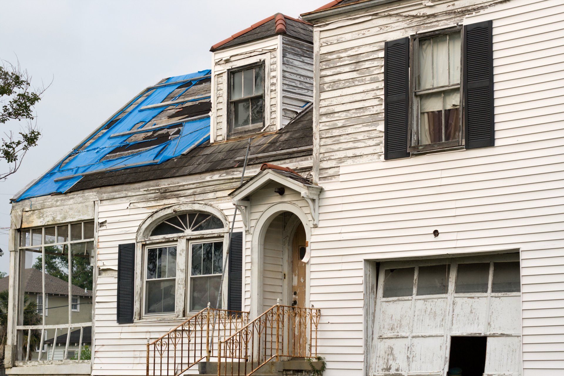 An old white house with a blue tarp on the roof.