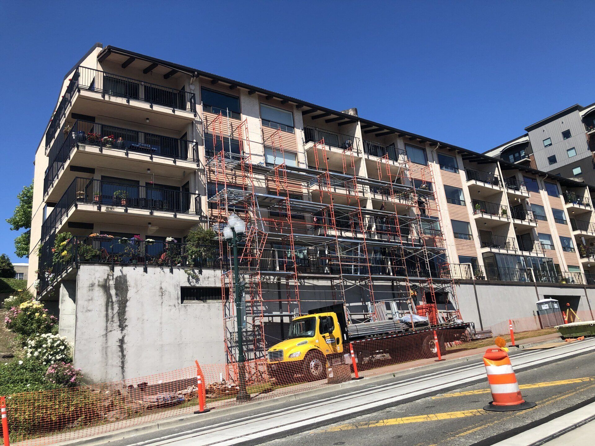 A large building under construction with scaffolding and a yellow truck parked in front of it.