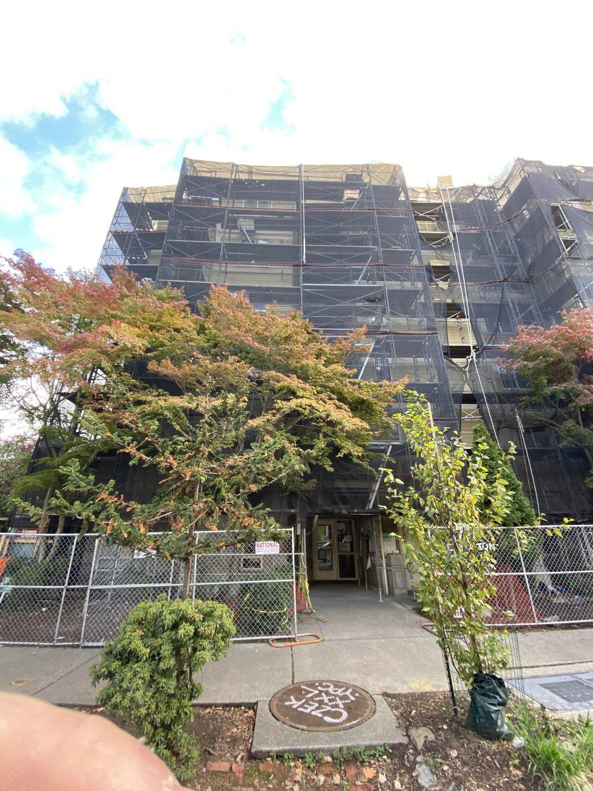 A large building under construction with scaffolding and trees in front of it.