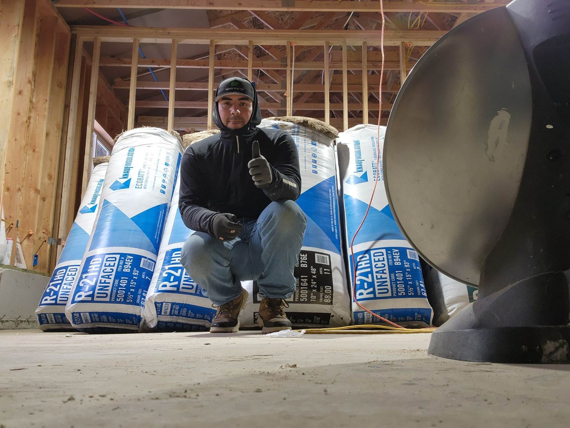 A man is kneeling in front of a pile of insulation and giving a thumbs up.