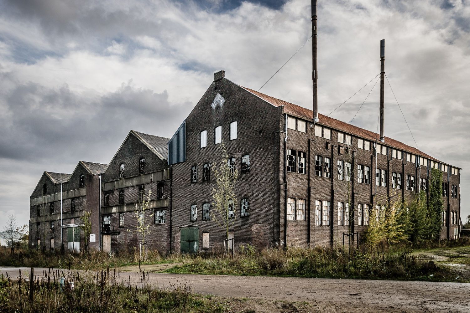 A large brick building with a lot of windows is sitting in the middle of a field.