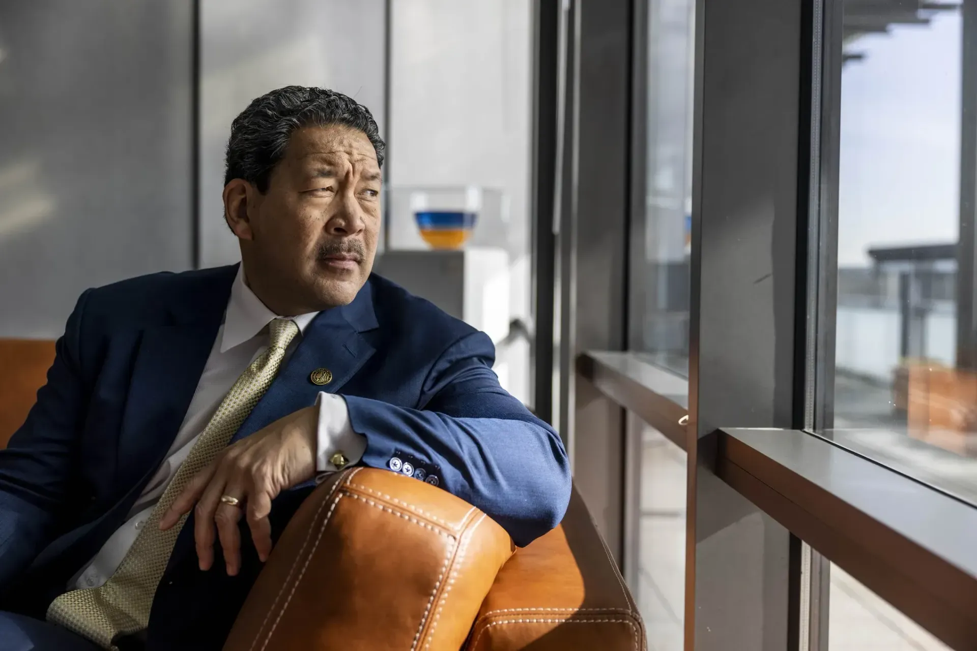 A man in a suit and tie is sitting on a couch in front of a window.