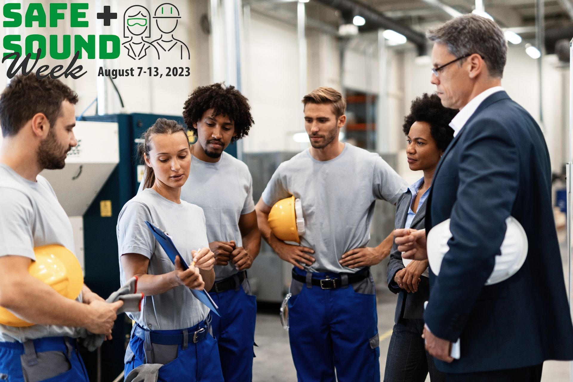 A group of construction workers are standing in a factory talking to a man in a suit.