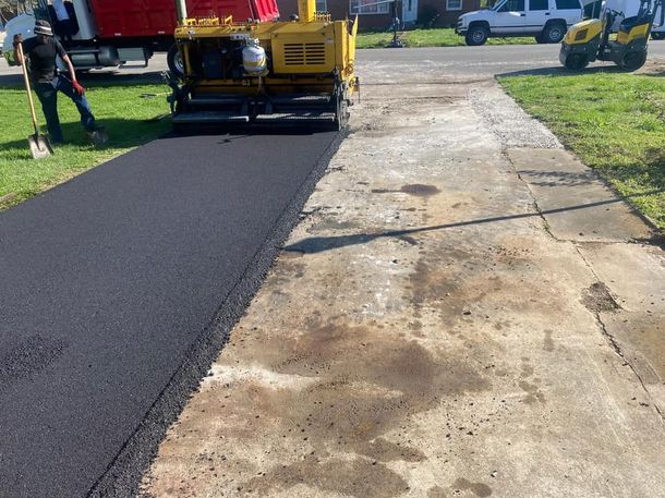 A man is standing next to a machine that is laying asphalt on a sidewalk.