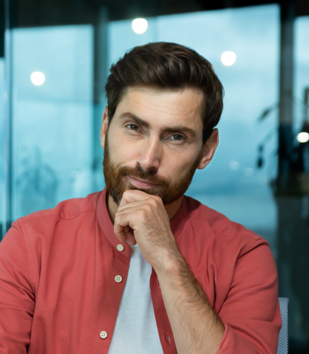 A man with a beard is sitting with his hand on his chin.