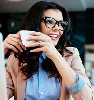 A woman wearing glasses is drinking a cup of coffee.