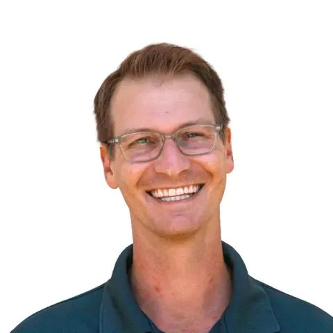 Man with glasses smiling, wearing a teal collared shirt, against a white background.