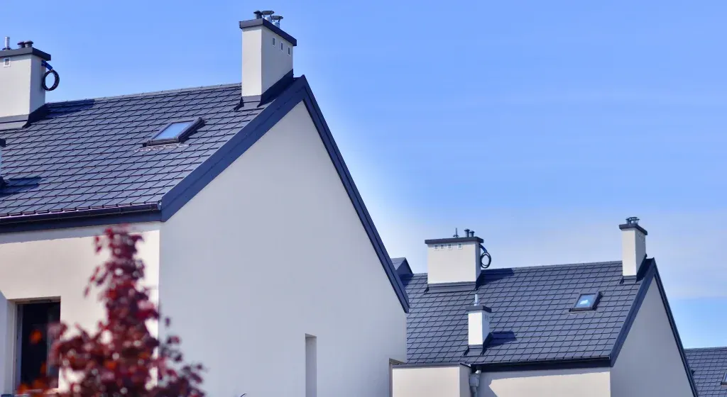 Row of white houses with dark gray roofs, blue sky.