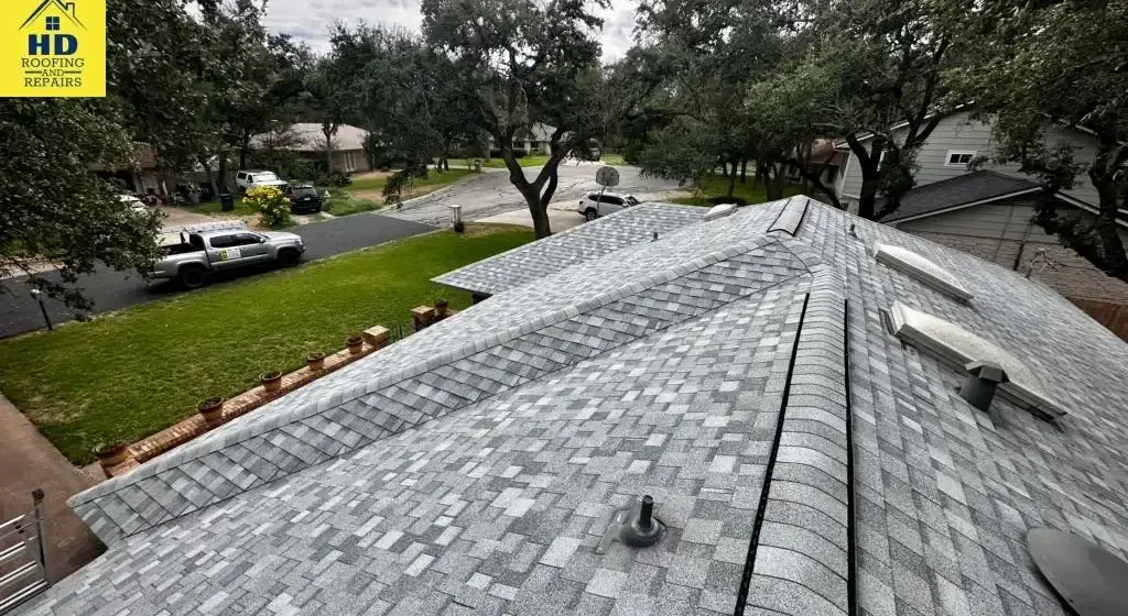 A gray asphalt shingle roof on a house with skylights and an adjacent green yard, trees, and a street.