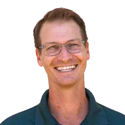 Man wearing glasses smiling. He's wearing a dark green shirt. Yellow background.