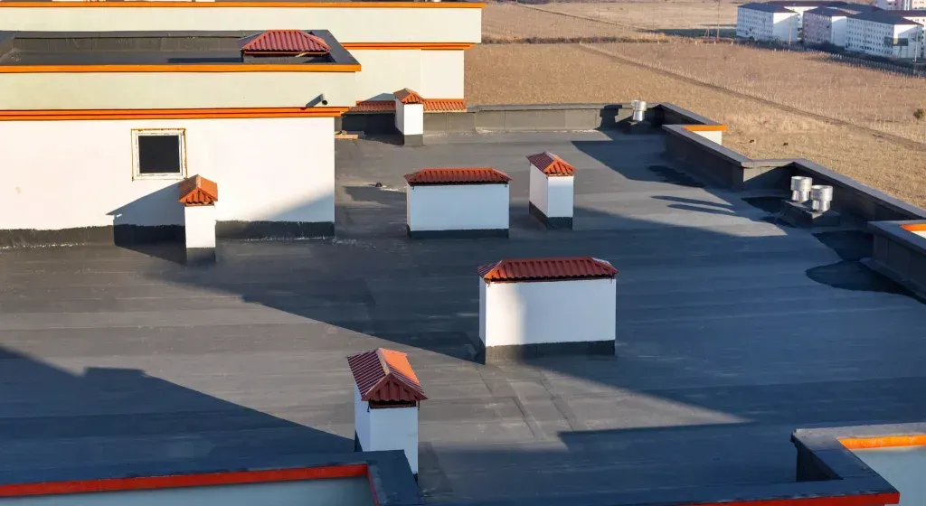 Flat rooftop with white structures and red-tiled caps, black roof surface.