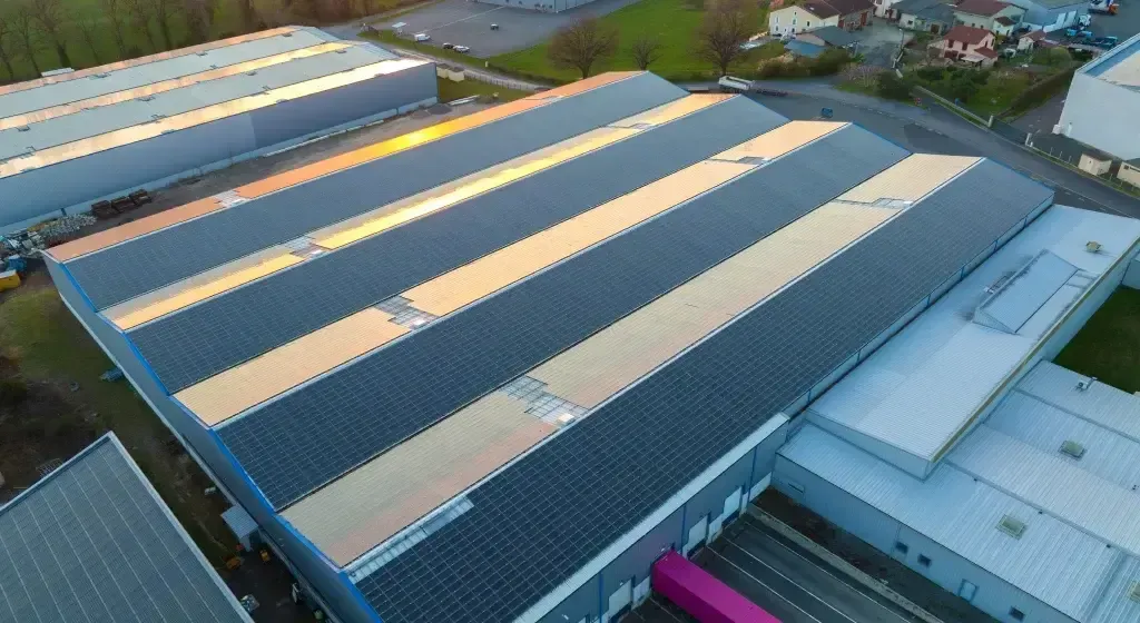 Aerial view of industrial buildings with corrugated metal roofs reflecting sunlight.