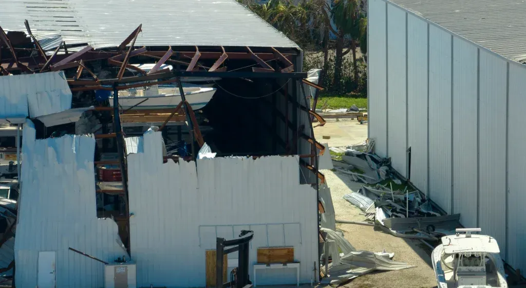 Damaged building with missing walls and roof; debris scattered. Boat in foreground.