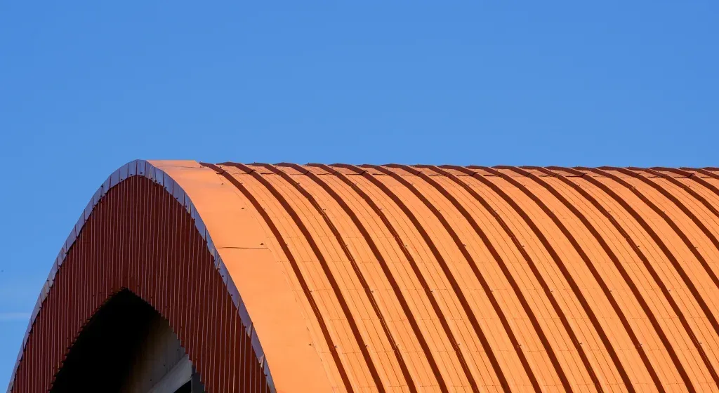 Curved orange metal roof against a bright blue sky.