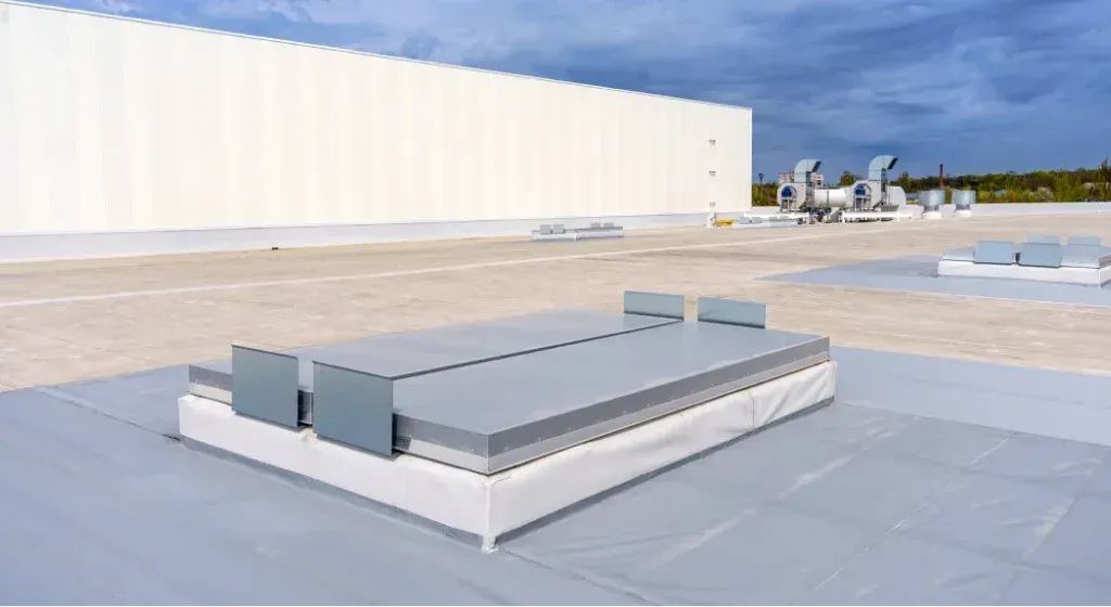 A flat, light gray commercial roof with air conditioning units and a large white wall.
