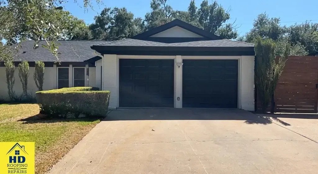 A single-story house with a two-car garage, black roof, and white exterior; driveway and landscaping.