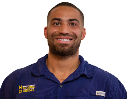 Man in blue shirt smiling, wearing a necklace. The shirt has a pocket with logo.
