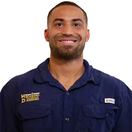 Man in blue shirt smiling, wearing a necklace. The shirt has a pocket with logo.