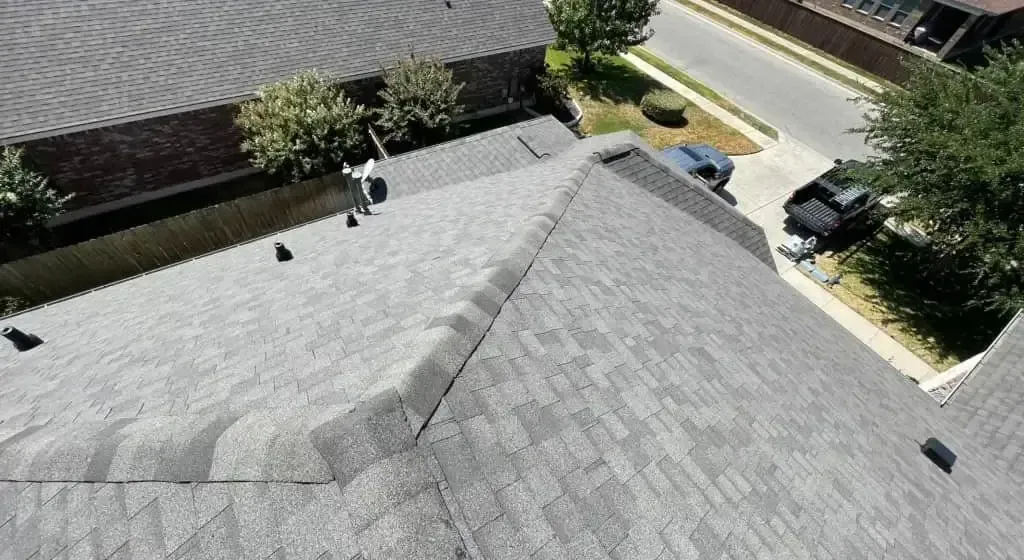 Overhead view of a gray shingled roof with a person, possibly a roofer, and a street with cars.
