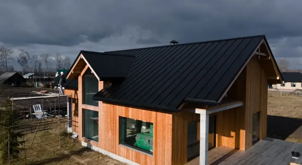 Wooden house with black roof under cloudy sky.