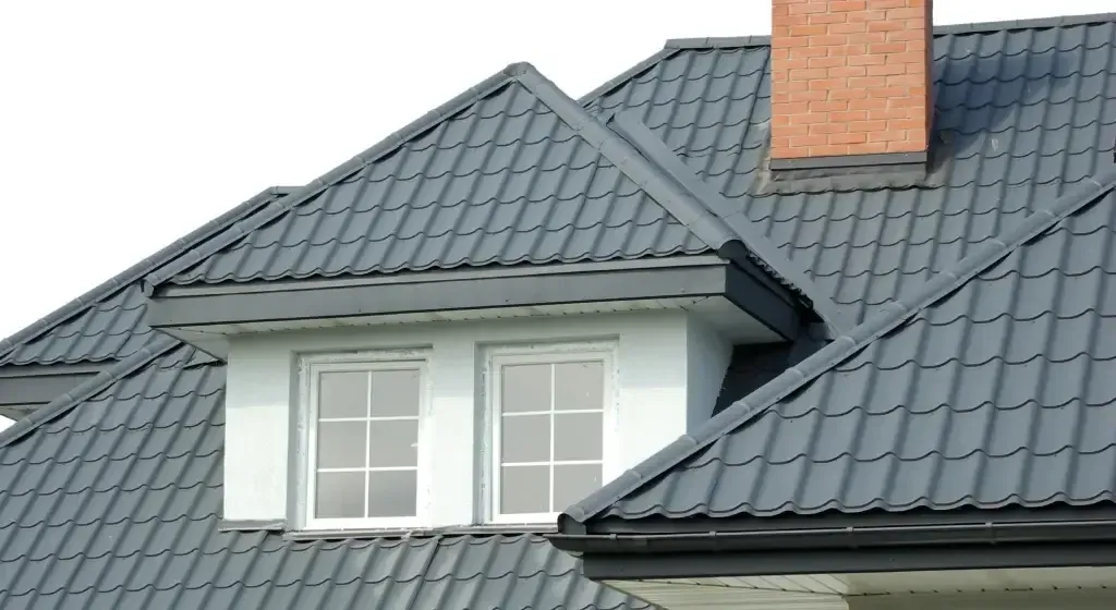 Gray metal roof on a white building with two windows and a brick chimney.