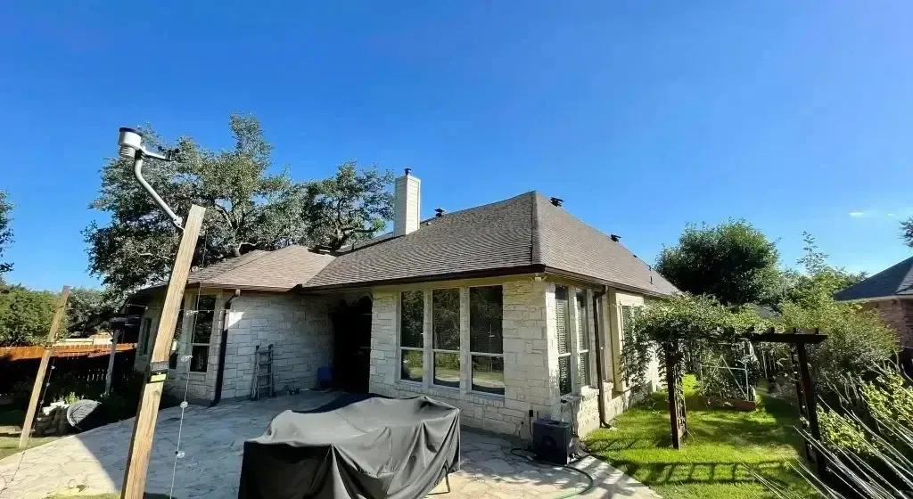 House with a brown roof, brick exterior, and windows under a bright blue sky.