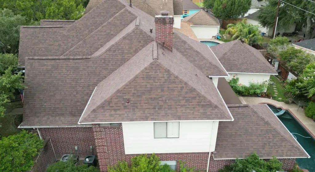 Aerial view of a brown-roofed house with a brick exterior, a chimney, and a swimming pool.