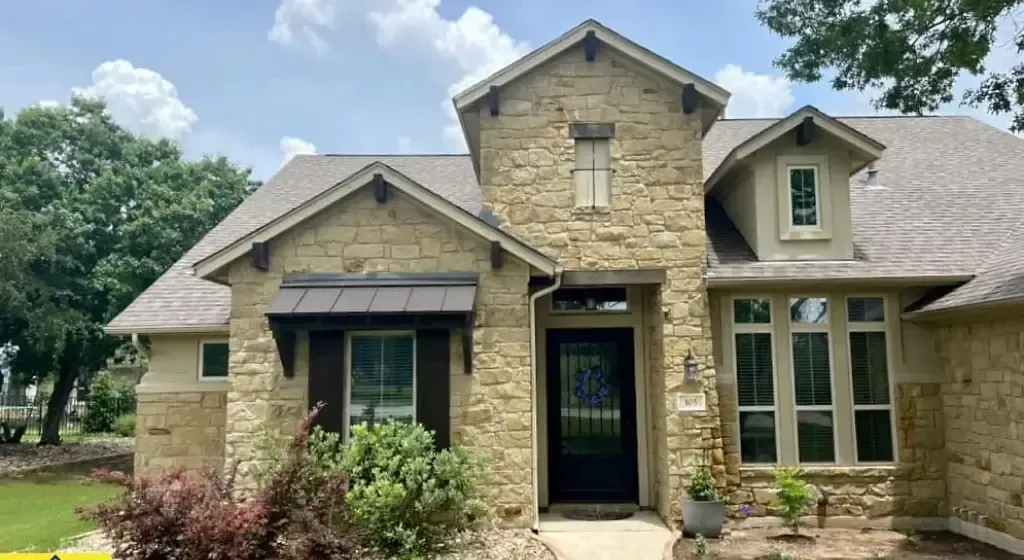 Stone-clad house with a black door, brown roof, and dark brown window shutters under a blue sky.