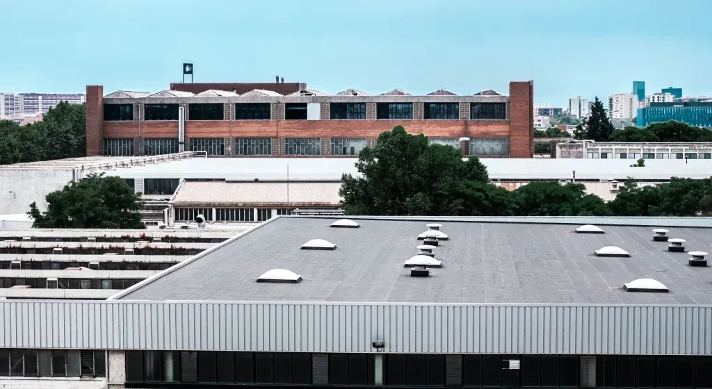 Roofs of industrial buildings against a light blue sky; a brick building is in the background.