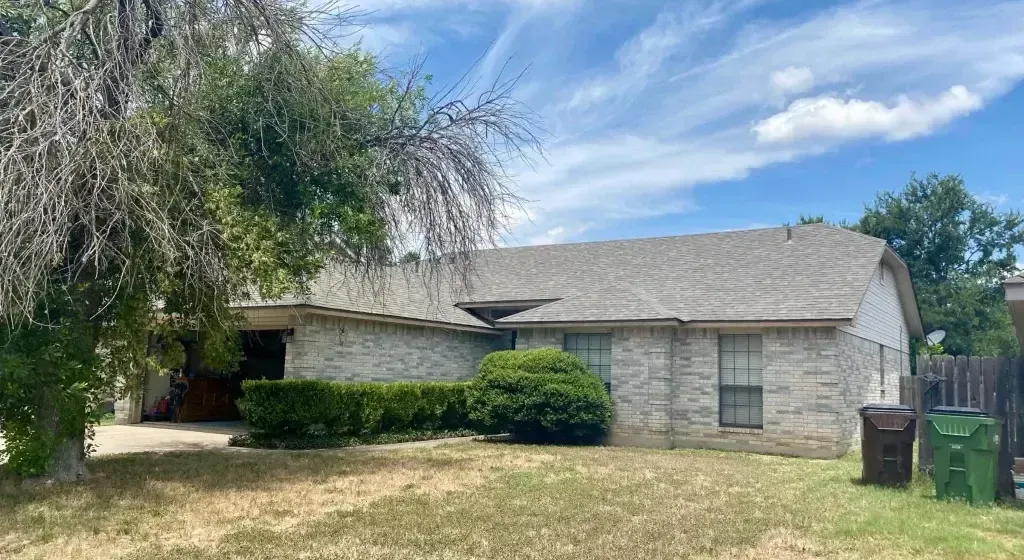 Residential house with light brick exterior, visible roof, and front yard.