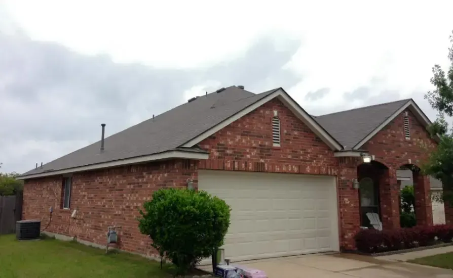 Brick house with a gray roof and white garage door under a cloudy sky.