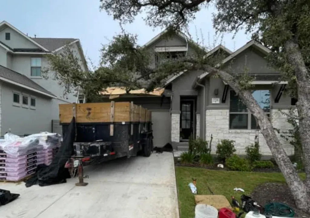 House with a trailer in driveway; construction materials are present, indicating a roof project.