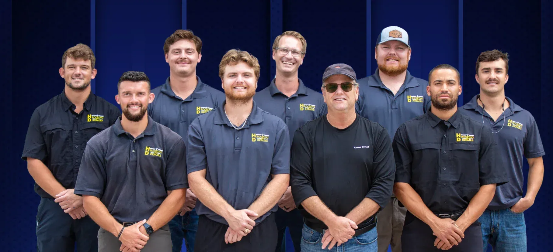 A group of ten people wearing matching work shirts posing for a photo against a blue background.