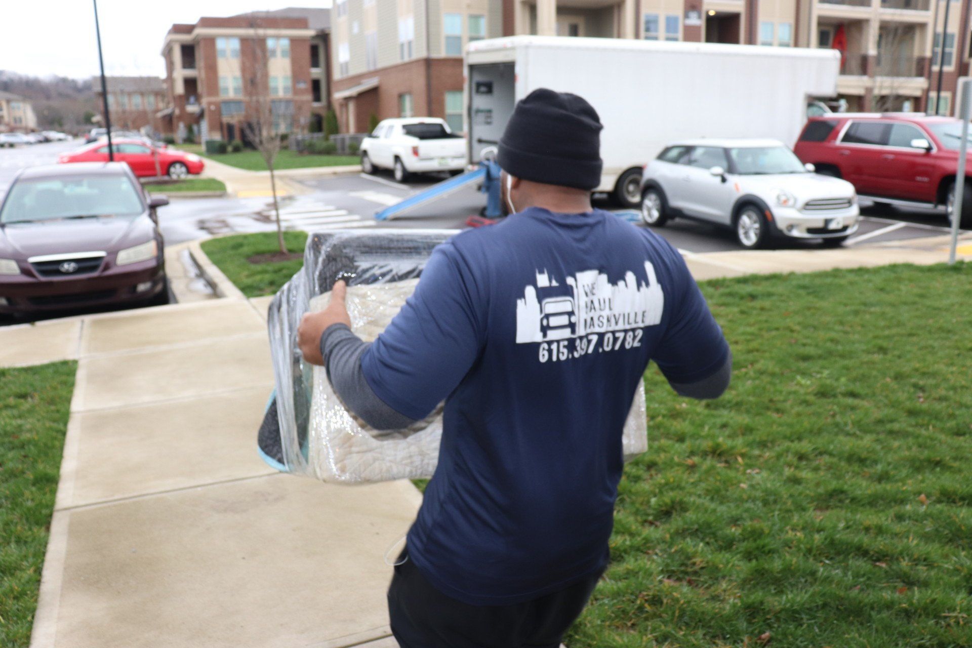 A man in a blue shirt is carrying a box on a sidewalk.