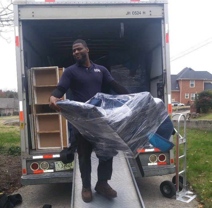 A man in a blue shirt is carrying a chair wrapped in plastic
