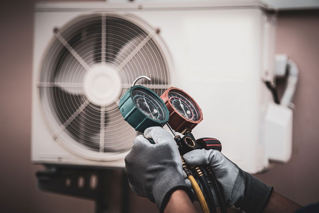 A person is holding two gauges in front of an air conditioner.