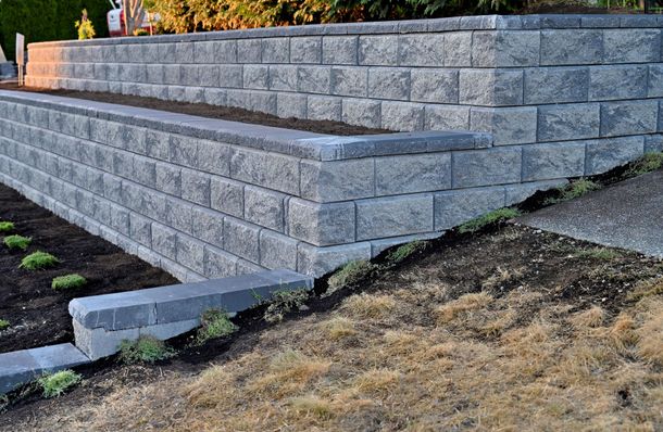 Gray block retaining wall in a yard, holding back earth and supporting a garden.